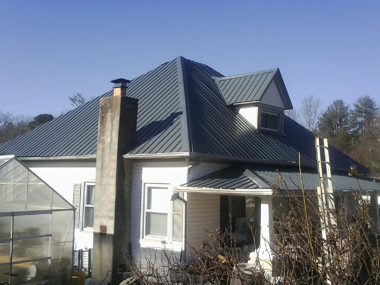 Dark blue standing seam metal roof on a white farmhouse with dormer — Slate & Tile Roof Repair by Roofing Brothers in Bellflower