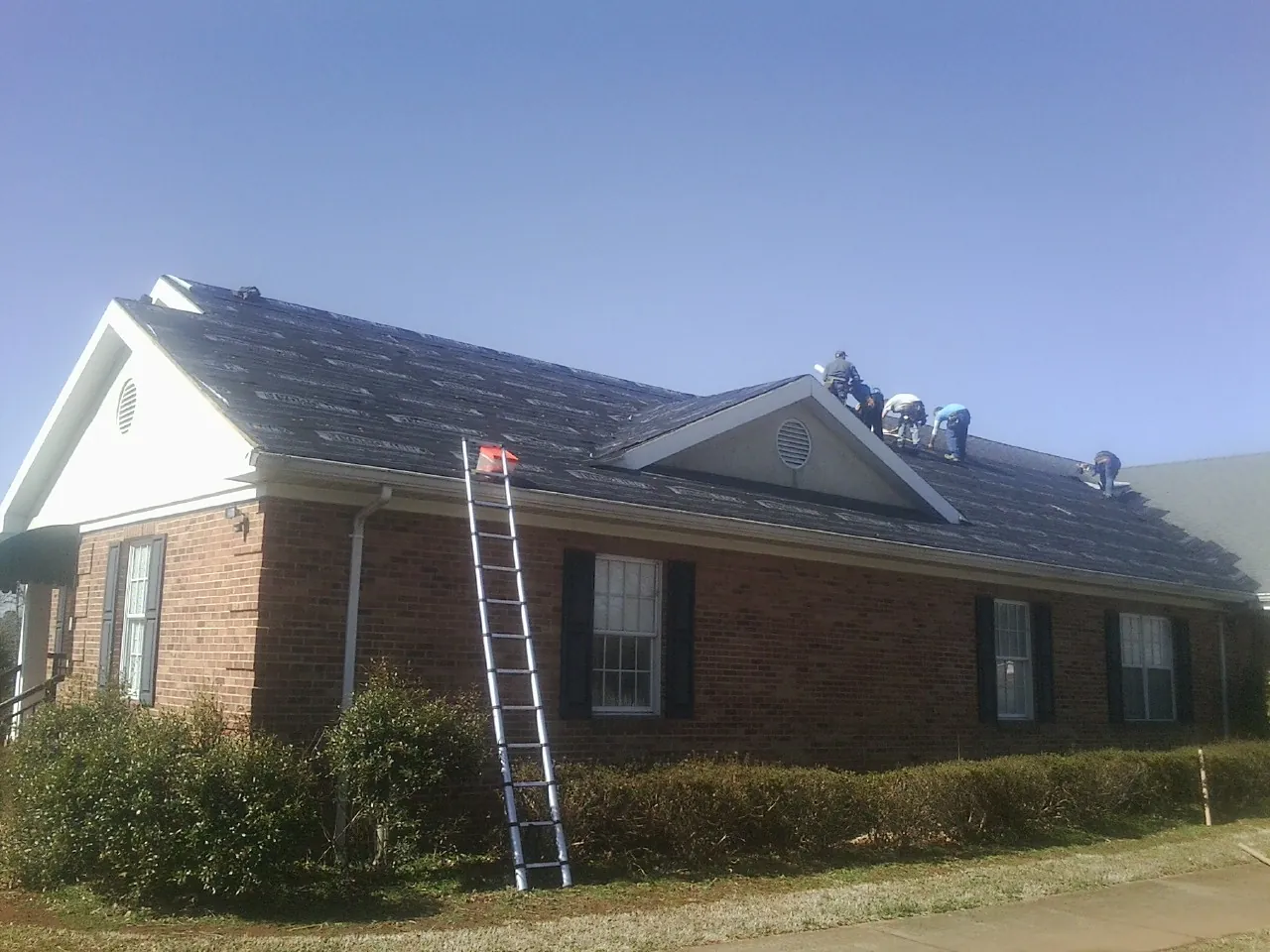 Crew tearing shingles off a brick ranch roof with a ladder set — Emergency Roof Repair work by our crew in Bellflower