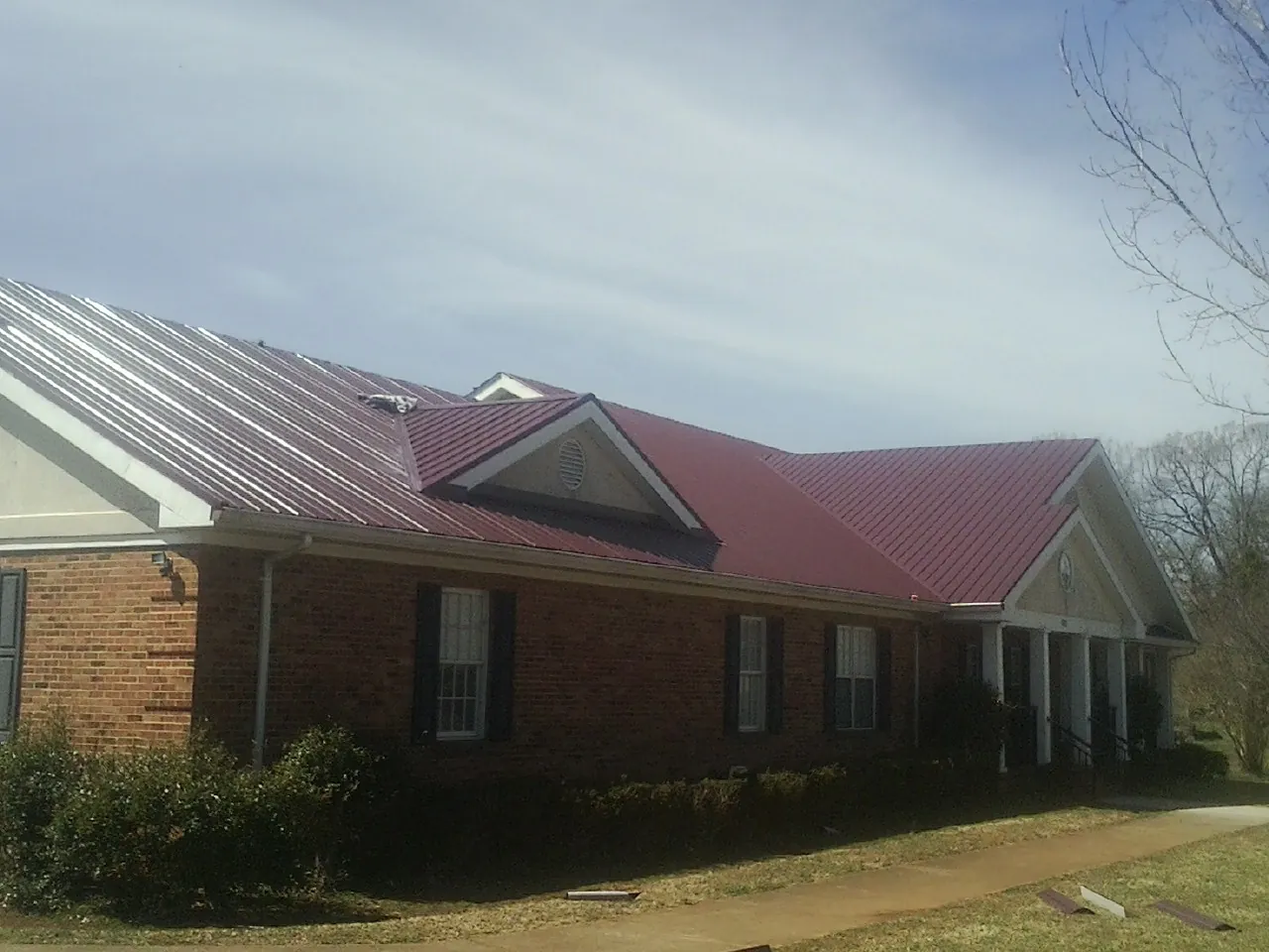 Red metal roof with gabled entries on a long brick building, from a Hail Damage Roof Repair job in Bellflower