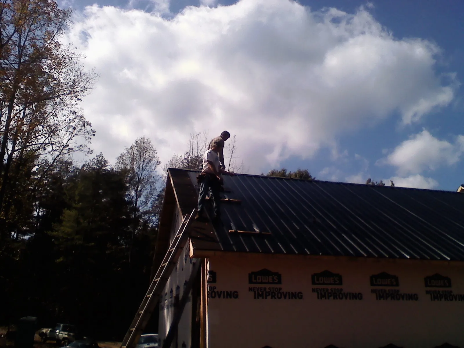 Roofer fastening dark metal panels high against a cloudy sky, from a Roof Inspection job in Bellflower