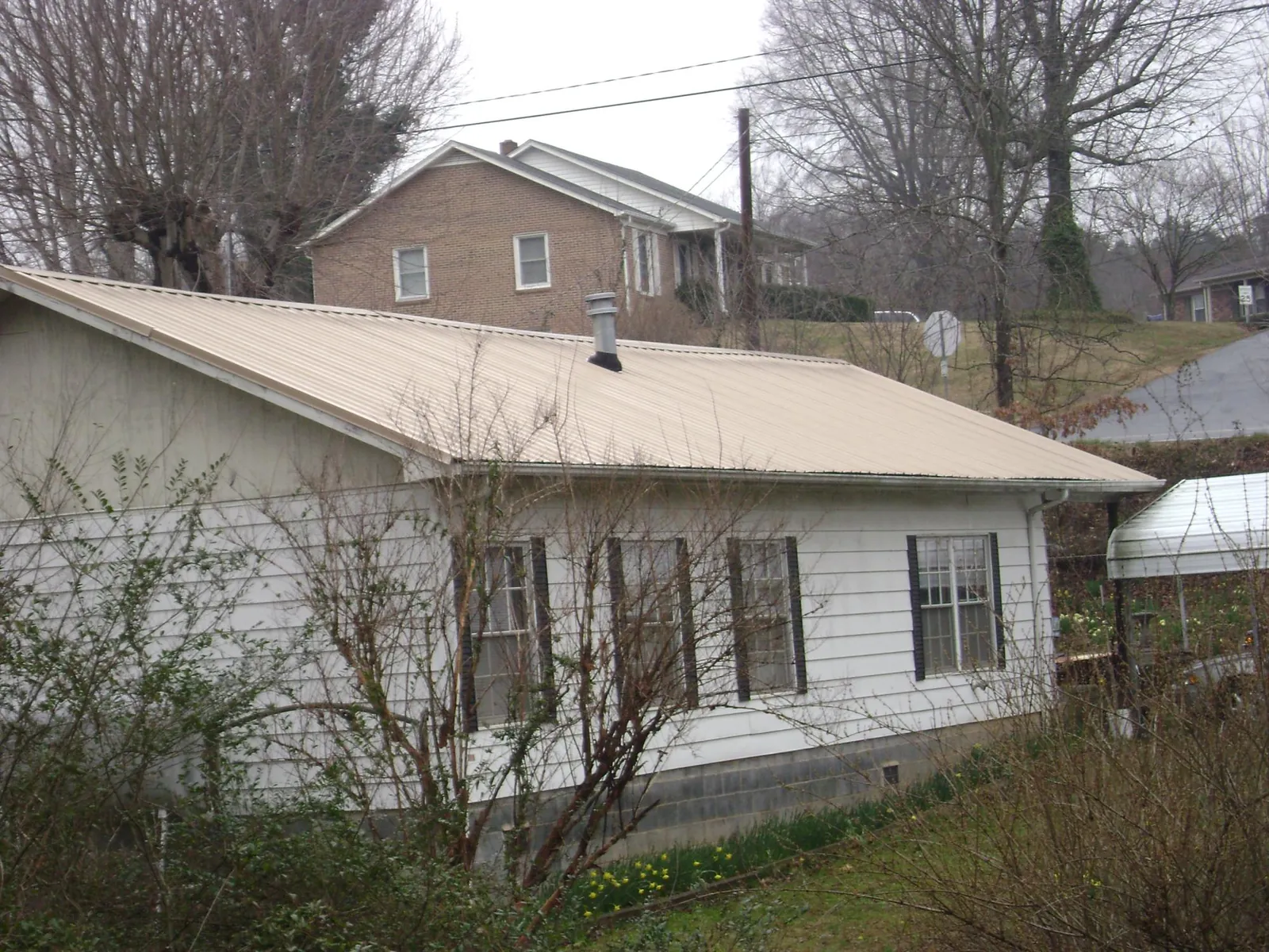 Tan metal roof on a white sided house set into a hillside — Commercial Roofing by Roofing Brothers in Bellflower