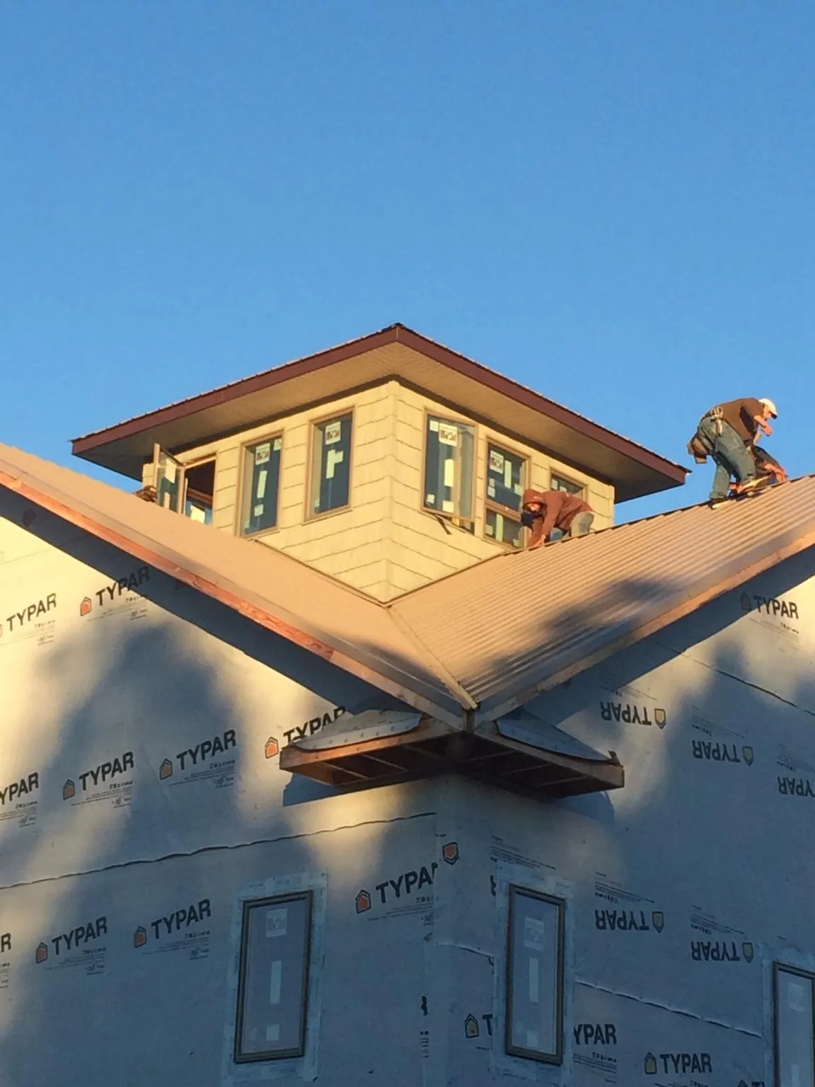 Roofers working around a rooftop cupola on a new metal roof at sunset — Roof Waterproofing in Bellflower by Roofing Brothers